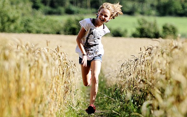Flicka som springer i ett sädesfält